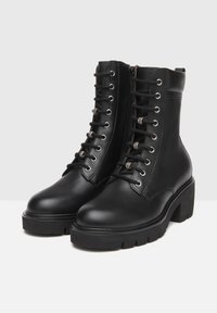 Bottines en cuir noir avec un bout arrondi, un lacet à l'avant, des œillets en métal argenté et une semelle épaisse. Texturées sur la partie supérieure et inférieure.