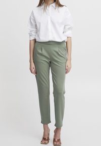 Jasnozielone, dopasowane spodnie z dwoma fałdami z przodu; zestawione z dopasowaną, białą koszulą z guzikami oraz brązowymi sandałami na obcasie.