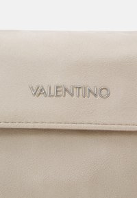 Beżowa skórzana torba o gładkiej fakturze, z klapą zakrywającą oraz srebrnym wytłoczonym na przodzie logo "VALENTINO".