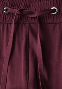 Bordowe szorty sportowe o miękkiej teksturze, elastyczny pas i sznurek z metalowym oczkiem w kolorze srebrnym oraz dopasowanym wiązaniem.