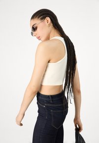 Top corto blanco de canalé combinado con jeans de talle alto azul oscuro. Gafas de sol negras con finos marcos plateados y un bolso negro liso.