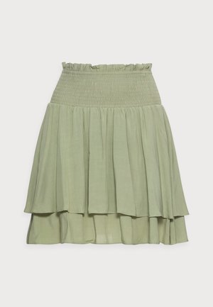 Jupe superposée vert clair avec ceinture élastique froncée et bord supérieur volantin contre un fond blanc.