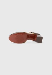 Scarpa con tacco alto in pelle marrone lucida con accenti beige a contrasto; suola in gomma testurizzata con motivo a righe circolari.