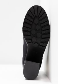 Semelle de botte en caoutchouc noir avec un motif texturé comprenant des grooves hexagonaux et linéaires. Le talon est massif avec une finition lisse.