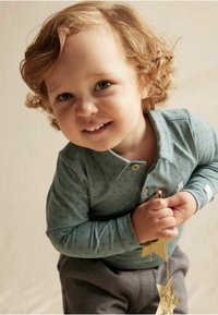 Valkoinen pitkähihaisen t-paita, jossa on kaulus ja tähtikuosi, yhdistettynä harmaisiin housuihin. Lapsi pitää kultaisia tähtikoristeita.