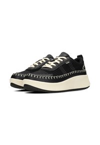 Zapatillas negras con parte superior de malla texturizada, costuras en crema que contrastan y una suela blanca gruesa, con cordones tradicionales y un collar acolchado.