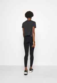 Black cropped t-shirt, short sleeves, paired with black leggings. Model wearing black athletic shoes with white accents. Simple, minimalist design.