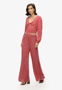 Conjunto de dos piezas en rojo y rosa con patrón, con manga larga, top corto y pantalones de pierna ancha; cintura elástica; textura de tela suave.