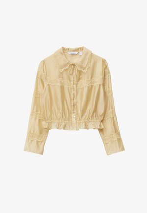 Cream blouse with a ruffled hem, long sleeves, lace accents, and a buttoned front. Features a pointed collar and ribbon tie at neckline.