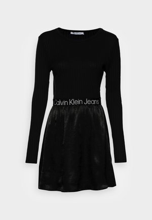 Vestido negro de manga larga con textura acanalada, top ajustado y falda acampanada, con una cintura brillante que lleva el logo "Calvin Klein Jeans".