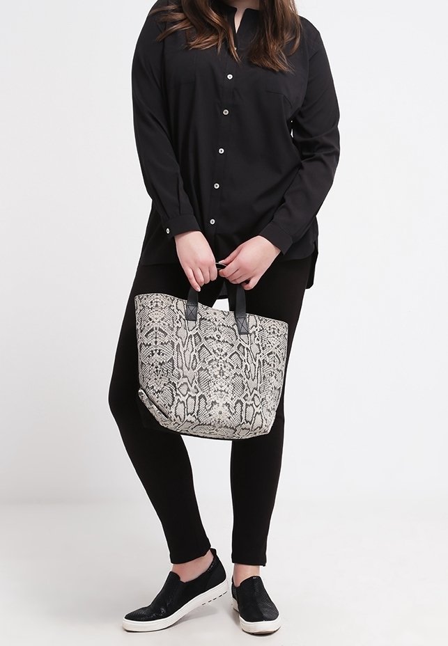 Czarna koszula zapinana na guziki, czarne legginsy i czarne buty wsuwane. Torba na ramię ma szary i czarny wzór w węża oraz solidne uchwyty.