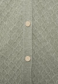 Lys grøn strikket cardigan med et tekstureret diamantmønster, fem karakteristiske knapper og ribbet detaljer langs fronten.