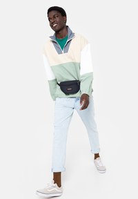 Pulovr s barevným blokem a vysokým límcem, obsahující mintovou zelenou, béžovou a šedou barvu. Spárovaný s světle modrými džíny a černým páskovým batohem.