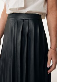 Gonna in pelle nera plissettata con una cintura liscia e una leggera lucentezza. La texture è morbida, evidenziata da pieghe ben stirate.
