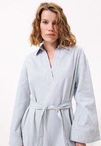Gestreiftes Hemdkleid in Hellblau und Weiß mit Kragen, halbem Knopfverschluss und weiten Ärmeln; inklusive eines gebundenen Taillengürtels. Weicher Stoff.