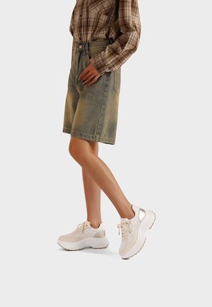 Shorts in denim chiaro con vita alta, abbinati a sneakers beige chiaro con dettagli in mesh e pelle. Camicia a maniche lunghe a quadri marrone.