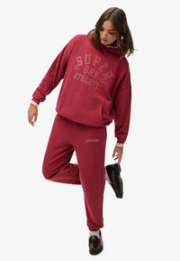 Bordowa bluza z kapturem i dresowe spodnie, wykonane z miękkiego materiału bawełnianego, z dużym wzorem logo. Bluza z kapturem i przednią kieszenią.