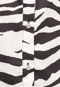 Ύφασμα με ασπρόμαυρο σχέδιο ζέβρας και δύο μικρά στρογγυλά κουμπιά από στρας ραμμένα σε μια κεντρική ραφή.