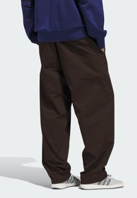 Καφέ παντελόνι με φαρδιά γραμμή και λείο υλικό, σε συνδυασμό με γκρι αθλητικά παπούτσια που έχουν τρεις ρίγες. Το πάνω μέρος είναι ένα μπλε φούτερ.