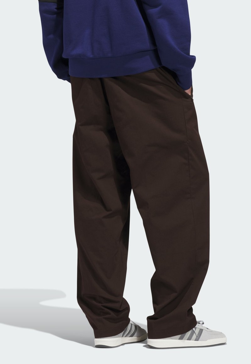 Pantaloni marroni a gamba larga con una consistenza liscia, abbinati a scarpe da ginnastica grigie con tre strisce. La parte superiore è una felpa blu.