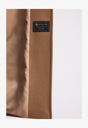 Wnętrze brązowego wełnianego płaszcza z czarną etykietą "Wool Collection Makalu Made in Poland" na jednolitym jasnym tle.