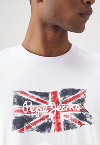 Witte katoen t-shirt met een grafiek van de Union Jack in rode, blauwe en witte kleuren. De weergegeven tekst bevat "Pepe Jeans London."