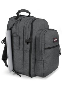 Mochila gris con múltiples compartimentos, tela texturada, correas acolchadas y un bolsillo lateral para un portátil. Se pueden ver los cierres de cremallera.