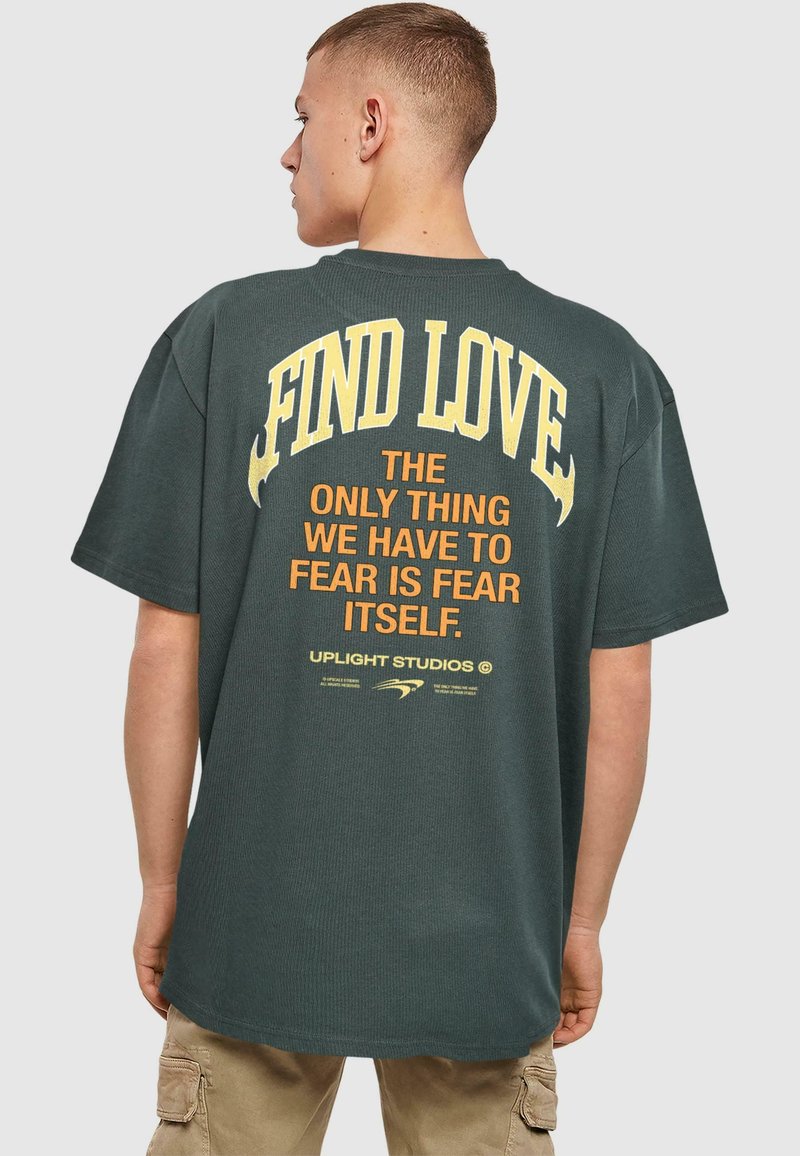 Mørkegrøn oversized T-shirt med stort gult og orange tekst på ryggen. Bomuldsstof med ribbet tekstur og afslappet pasform.