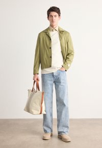 Lichtgroene jas met zwarte knopen over een crèmekleurige trui, gecombineerd met blauwe denim jeans. Bruin handtas met grijze strepen. Beige schoenen.