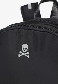 Mochila negra con textura suave, que presenta un diseño de calavera y huesos cruzados en plata, una cremallera duradera y una tira reflectante en la parte superior.