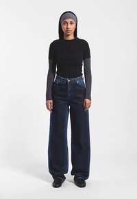 Svart kortärmad topp lager-på-lager över en grå långärmad skjorta, kombinerad med högt midjade mörka vida jeans och svarta skor.