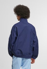 Námornícky modrá, nadrozmerná bunda vyrobená z ľahkého materiálu, s vysokým golierom, elastickým lemom a bočným švom.