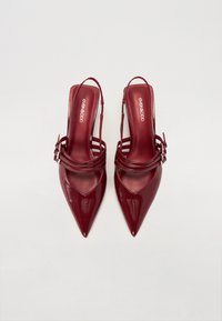 Burgundia läikiv nahk slingback kontsad terava nina, pahkluu rihmade ja kihiga põhjadega. Bränding nähtav sisetallal.