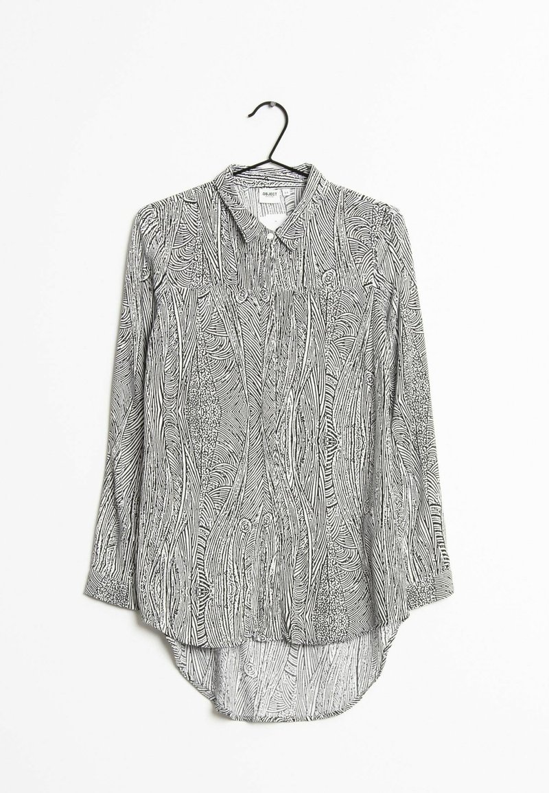 Blouse à manches longues noire et blanche à boutons, avec des motifs abstraits en lignes ondulées, suspendue à un cintre noir sur un fond blanc.