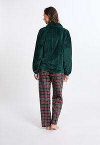 Zelený fleecový svetr s vysokým límcem, doplněný červenobílými károvanými kalhotami. Kalhoty mají volný střih a rovné nohavice.