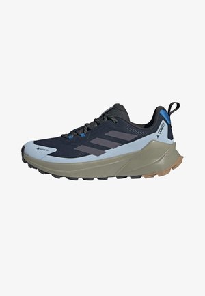 Zapato de senderismo Adidas Terrex negro y gris con suela beige, lengüeta azul en el talón, cordones negros y etiqueta impermeable Gore-Tex en la puntera.