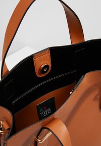 Sac à main ouvert en cuir couleur tan avec intérieur noir, fermeture à pression magnétique et poche intérieure visible étiquetée "even & odd".