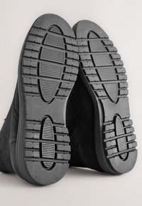 Schwarze Wildleder-Stiefeletten mit Gummisohlen. Das Profil verfügt über horizontale und vertikale Rillen für besseren Halt. Seitlicher Reißverschluss an jedem Stiefel.