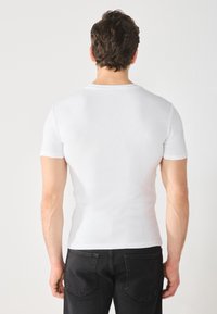 Bílý krátký rukáv, přiléhavé tričko s kulatým výstřihem, spárované s tmavými džínami. Hladk�á textura, minimalistický design, bez vzorů.