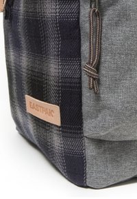 Marinblå och grå ryggsäck med rutigt mönster, texturerad tyg och en läder EASTPAK logotagg på framsidan. Försedd med en flätad dragkedjehantering.