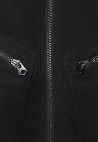 Zwarte stof met centrale zilveren rits en twee schuine zilveren ritstasjes met stofstikseldetails.