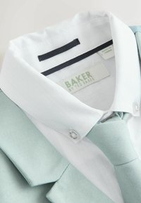 Svetlo modro obleko z teksturirano tkanino, belo srajco s subtilnim vzorcem in ujemajočo se kravato. Oznake so vidne na ovratniku in kravati.