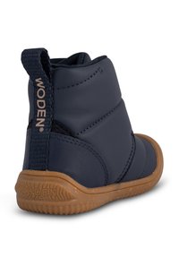 Bota impermeable de color azul marino con parte superior acolchada, paneles laterales elásticos, tirador trasero y suela de goma texturizada. Logotipo en la parte posterior.