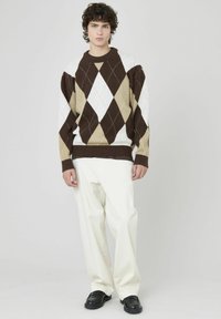Pull en argyle marron, blanc et beige avec un col rond, associé à un pantalon blanc et des chaussures noires. Texture en tricot confortable.