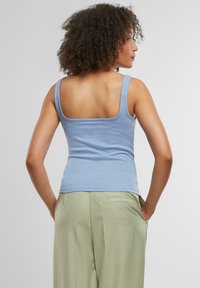 Top de tirantes acanalado de color azul claro con espalda cuadrada, tirantes delgados y silueta ajustada, combinado con pantalones holgados de color verde pálido.