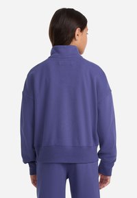Sudadera oversized morada con cuello alto, hecha de tela suave. Presenta hombros caídos y un dobladillo recortado, ofreciendo un ajuste relajado.