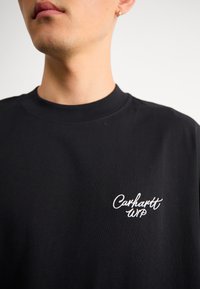 Crna pamučna majica s okruglim izrezom i kratkim rukavima. Sadrži bijeli izvezeni logo "Carhartt WIP" na prsima. Glatka tekstura.