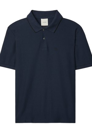 Tamsiai mėlynas trumpomis rankovėmis polo marškinėliai su dviem sagomis, apsiūtas apykakle su plona juoda apvija ir mažu „ck“ logotipu kairėje krūtinės pusėje.