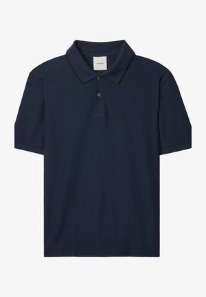 Tamsiai mėlynas trumpomis rankovėmis polo marškinėliai su dviem sagomis, apsiūtas apykakle su plona juoda apvija ir mažu „ck“ logotipu kairėje krūtinės pusėje.