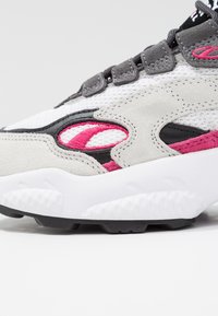 Sneaker grigio e bianco con upper in suede e mesh, caratterizzato da accenti rosa, pannelli testurizzati e una suola intermedia bianca ammortizzata con suola nera.